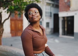 Cheerful young woman with curly hair and glasses smiling in a casual outfit.